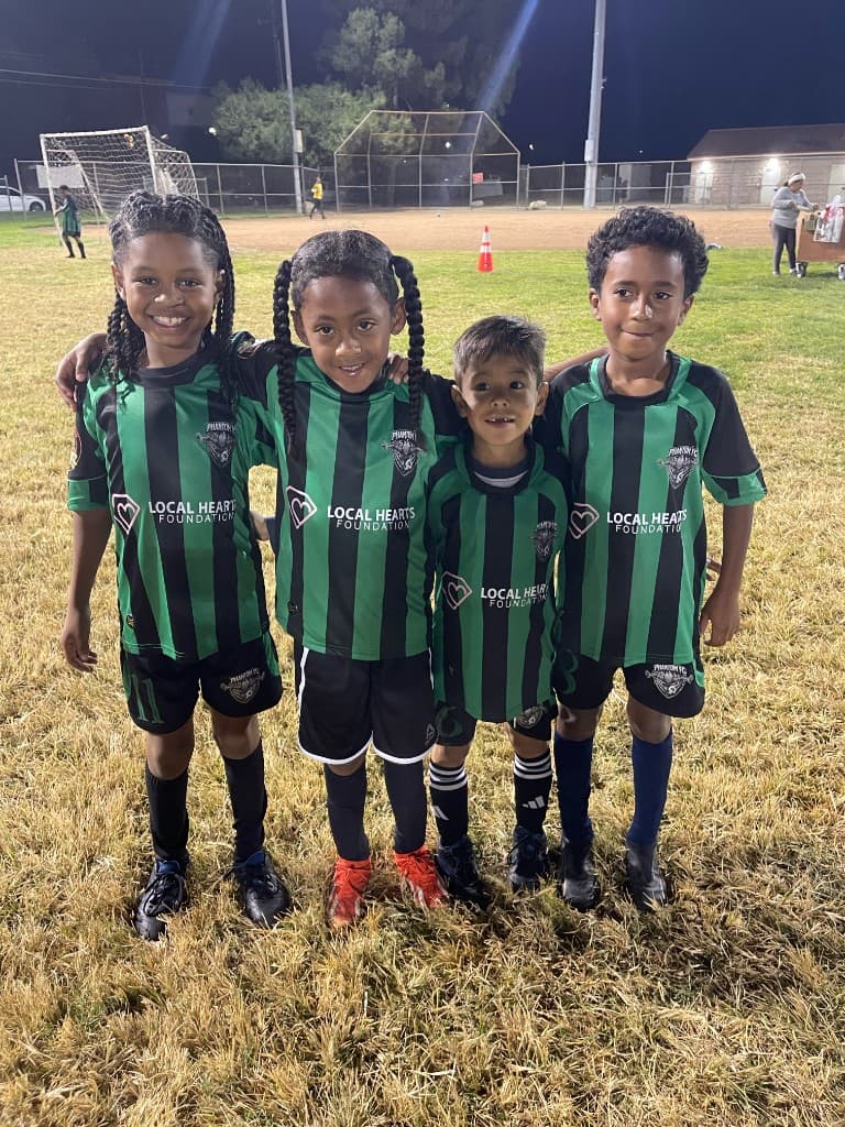 U7 teammates smiling with arms around each other in Local Hearts Foundation and Phantom FC kits
